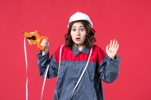 close-up-view-shocked-female-architect-uniform-wearing-hard-hat-with-measuring-tape-red-wall_140725-68443